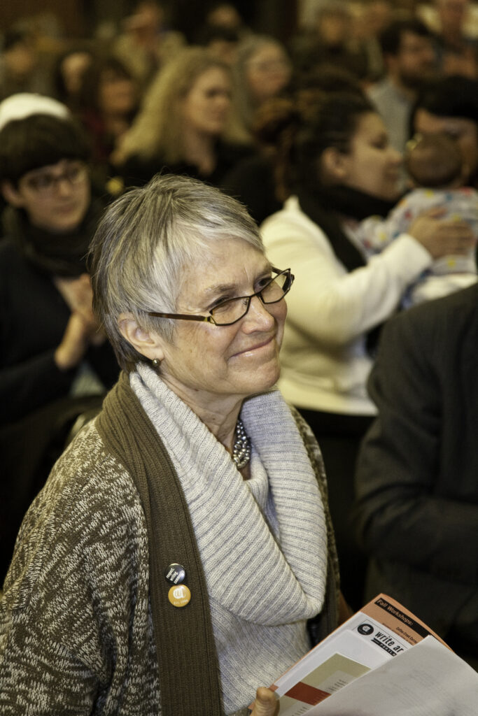 A woman with gray hair smiles in an audience of people.