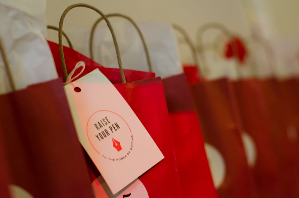 A line of red bags trails off into the distance. One bag has a tag tied to it with the words Raise Your Pen on it. 