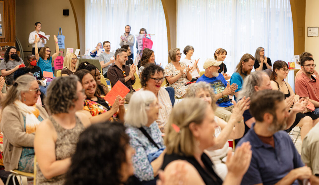 A crowd of people at a Reading clap and smile.