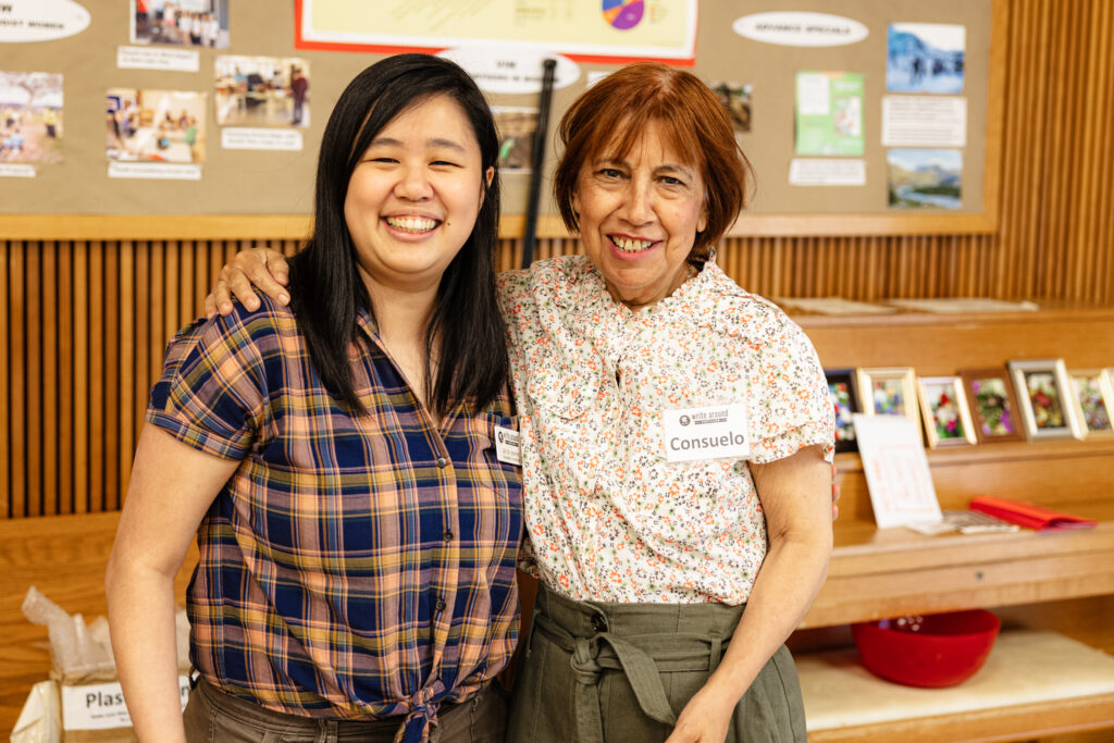 Two women of color stand together. One is younger and the other is older; the older woman has her arm around the younger one.