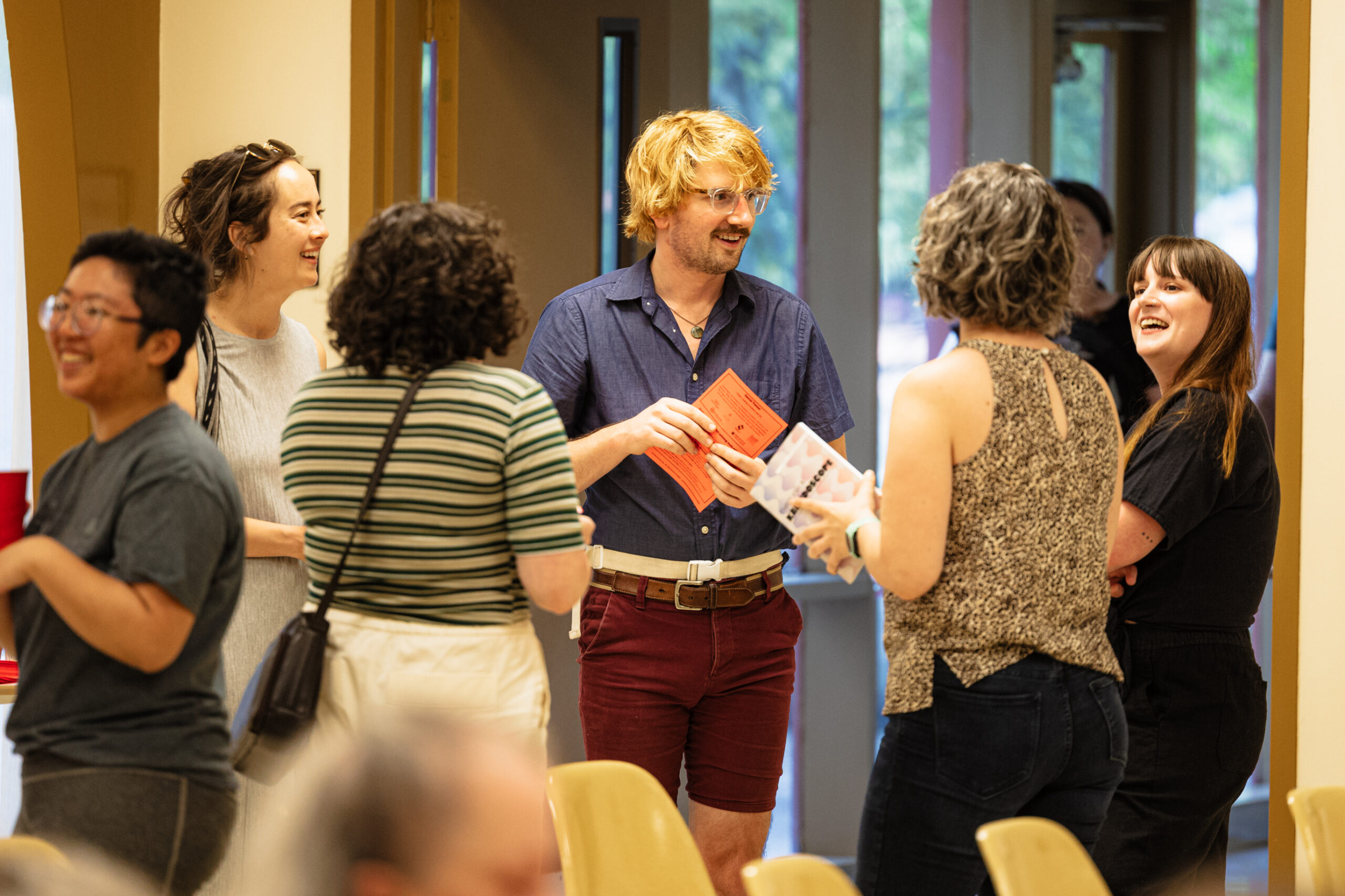 A group of people stand in a circle talking to each other. They smile and seem to be enjoying themselves.