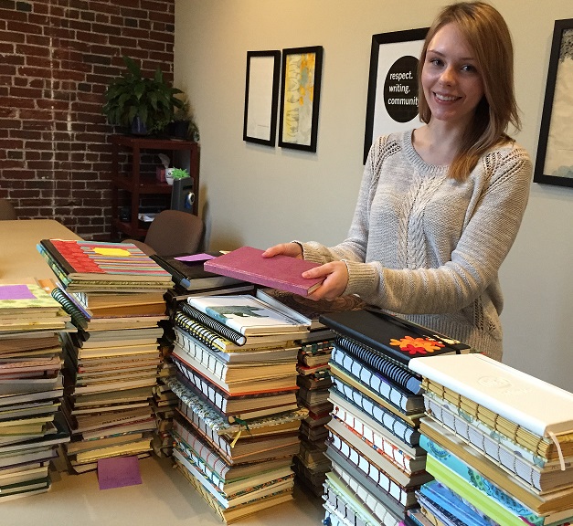 A woman stands in front of a large pile of journals in our office.