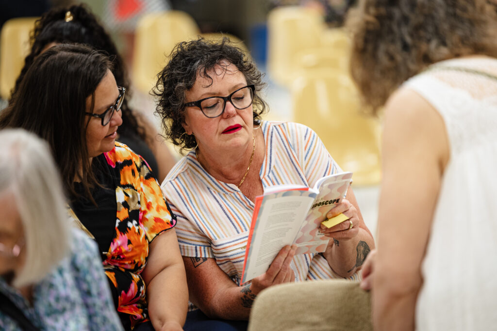 Two middle-aged women look at a book together.