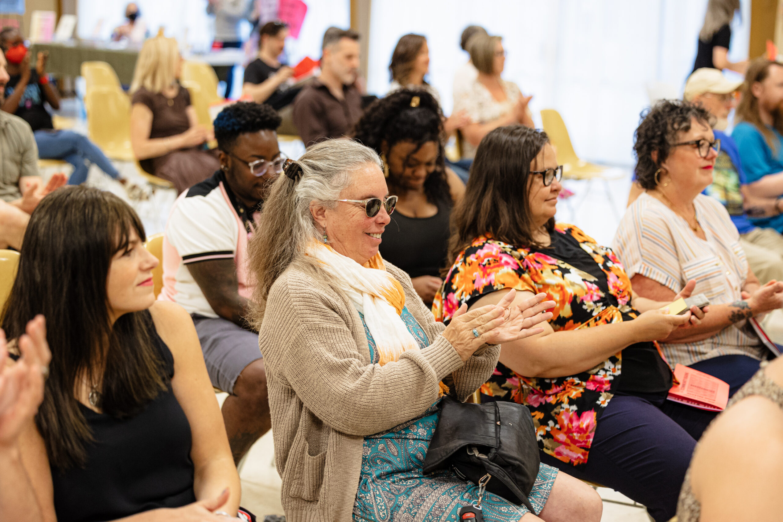 An audience of people of different ages, genders, and races sit at a Write Around Portland reading. Several are clapping