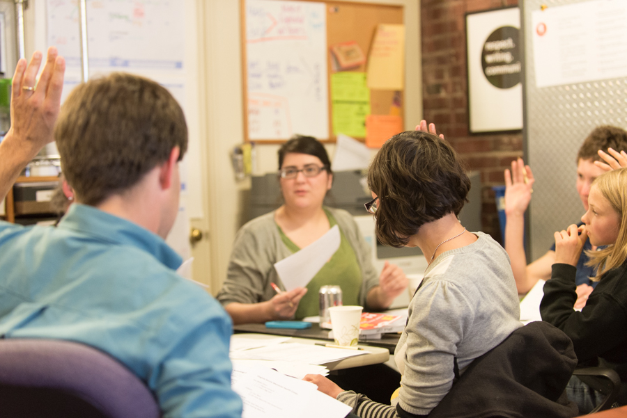 5 people sit around a table in our office. Some people are raising their hands.