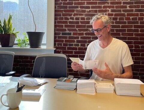 A man smiles as he puts together a mailing in our office.