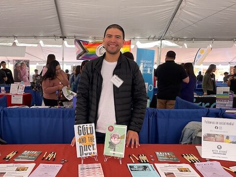A man stands in front of two of our books while helping out at a tabling event. 