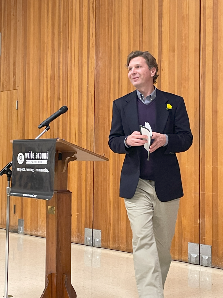 Moss Bittner approaches the podium after his creative writing workshop. He wears a dark suit jacket and sweater with khakis.