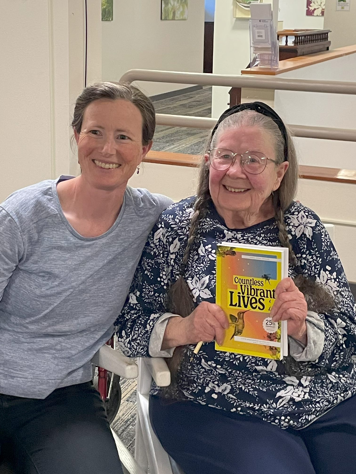 Two ladies of different generations sit together and pose with a copy of Write Around's anthology, Countless Vibrant Lives.